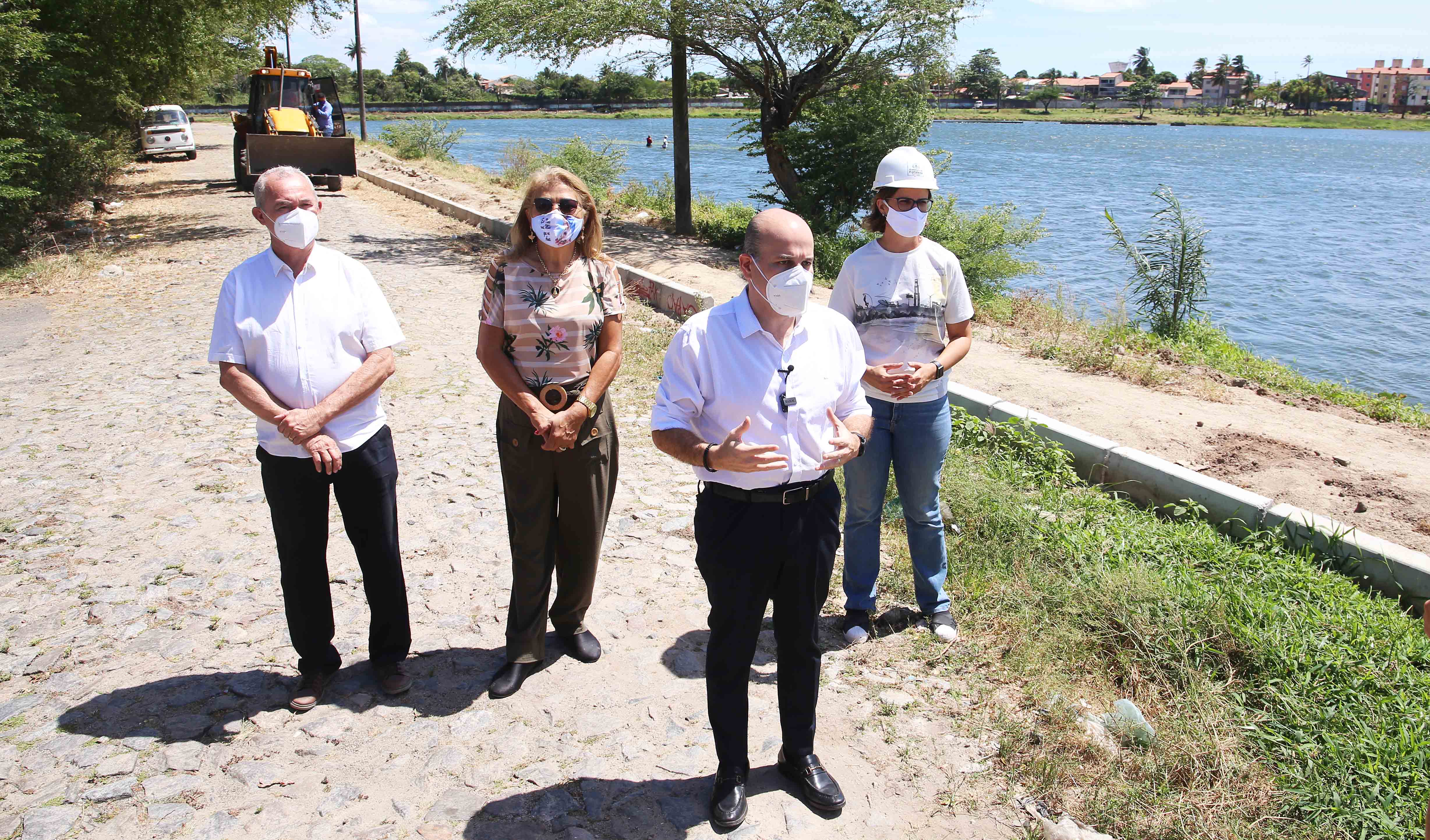 prefeito em pé com secretária Manuela, um senhor e uma senhor ao fundo, todos de máscara posando para a foto com a Lagoa do Mondubim ao fundo